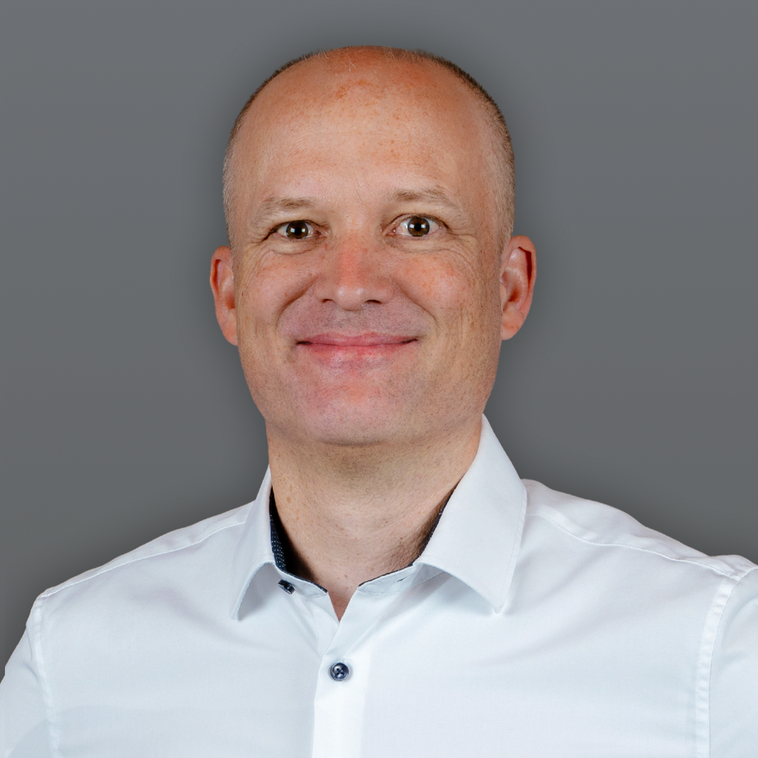 Portrait of Peter Kurz, Managing Director of itelio GmbH, wearing a white dress shirt against a grey backdrop.